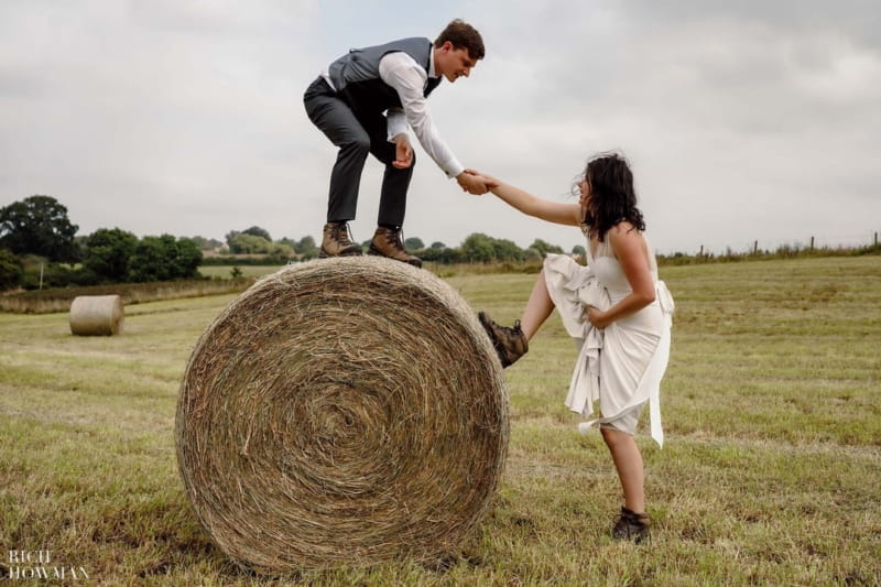 Groom holding bride's hand to help her climb up on to hay bale - Picture by Rich Howman