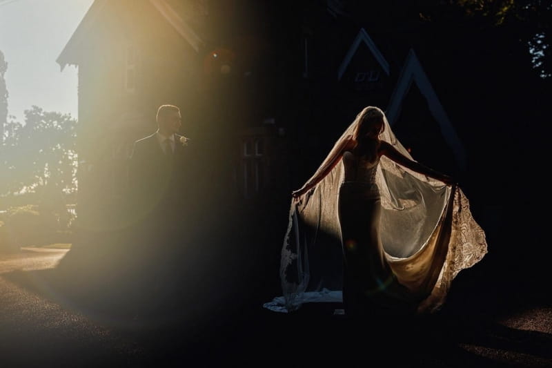 Bride and groom standing in shade, slightly lit by hazy sunshine - Picture by Steven Rooney Photography