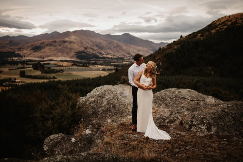 Bride and groom at the top of a hill with beautiful scenery behind them - Picture by Steph Newton Photography