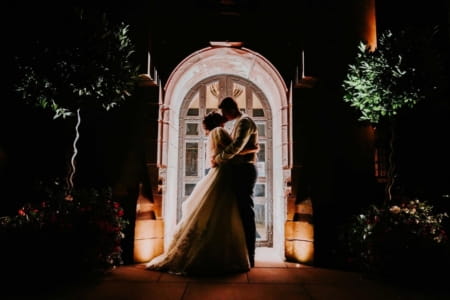 Bride and groom outside wedding venue at night, kissing in lit up doorway - Picture by Maddie Farris Photography