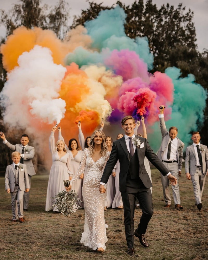 Bride and groom walking with brideal party behind then carrying colourful smoke bombs - Picture by Olegs Samsonovs Photography