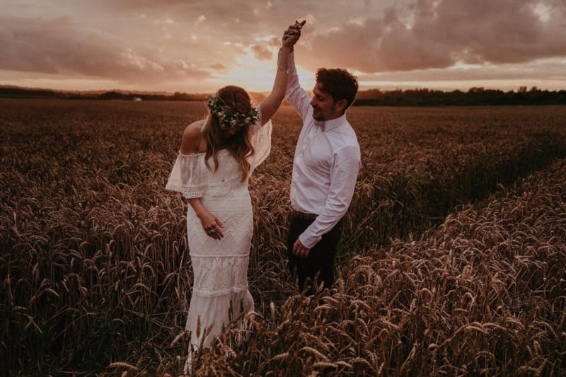 Bride holding groom's hand and twirling in corn field as sun sets - Picture by Jason Mark Harris